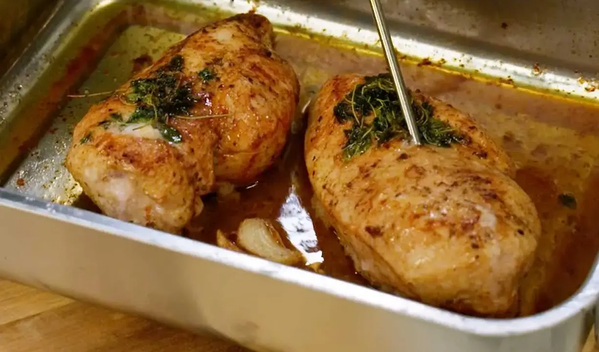 Två saftiga kycklingfiléer i ugnsform, redo för ett strimlad kyckling recept. En termometer mäter temperaturen.