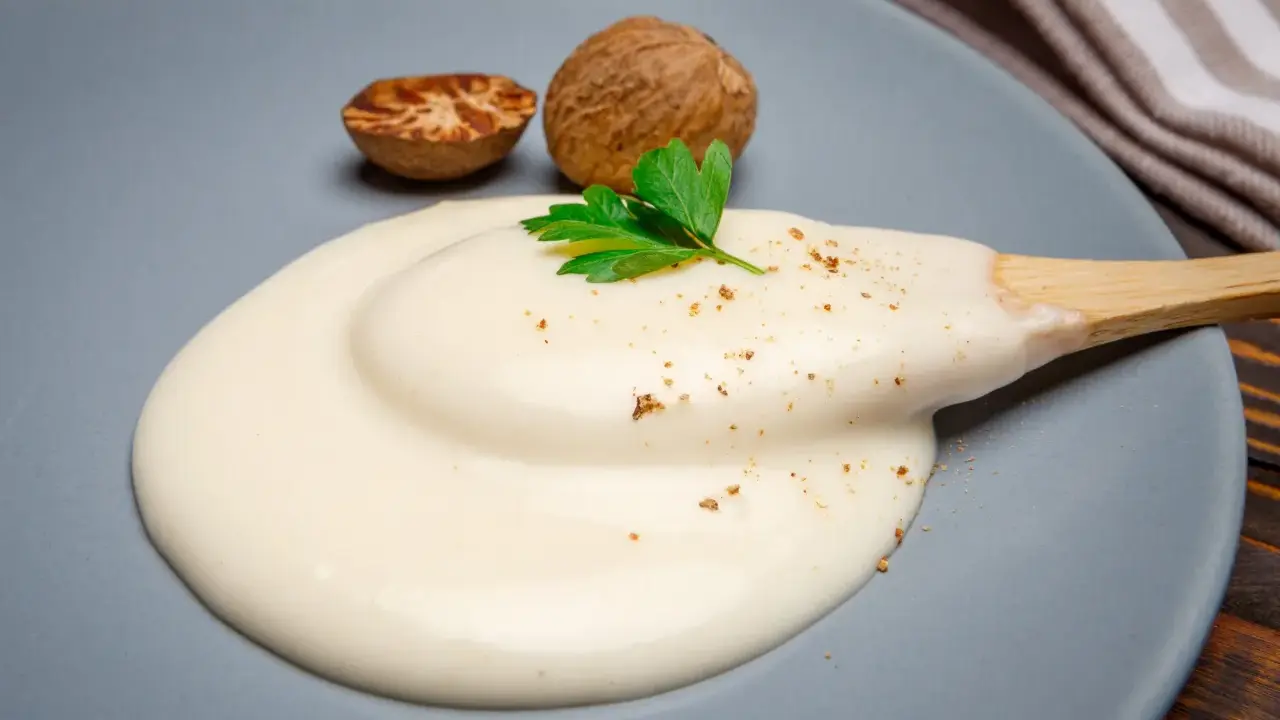 Krämig bechamelsås på en tallrik med muskotnötter och persilja. Perfekt för ditt bechamelsås recept.