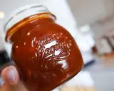 En hand håller ett glas med söt och syrlig rabarberchutney.