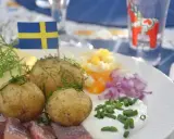 En tallrik med midsommar mat: sill, färskpotatis, ost, ägg och rödlök. En svensk flagga vajar stolt.