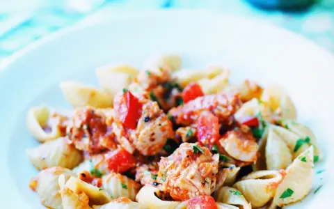 En närbild på en tallrik med tonfisksallad med pasta. Pastan är blandad med bitar av tonfisk, tomater och örter i en röd sås.