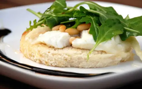 En bit rostat bröd med smält **chevre chaud**, pinjenötter och ruccola. En läcker förrätt.
