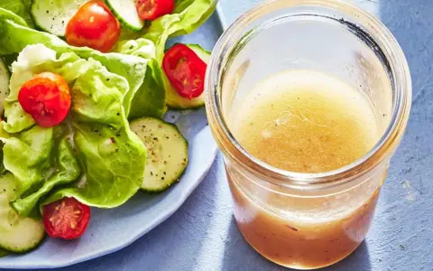 En burk med hemlagad salladsdressing bredvid en fräsch sallad med gurka och tomater. Ett perfekt salladsdressing recept för en lätt lunch.