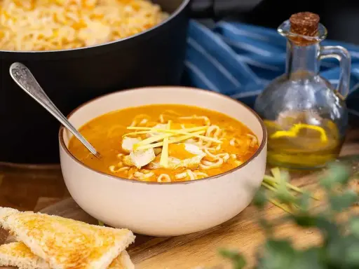 En skål med kycklingsoppa med nudlar och kycklingbitar, serverad med rostat bröd. Ett recept på kycklingsoppa som ser utsökt ut.