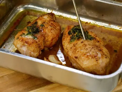 Två saftiga kycklingfiléer i ugnsform, redo för ett strimlad kyckling recept. En termometer mäter temperaturen.