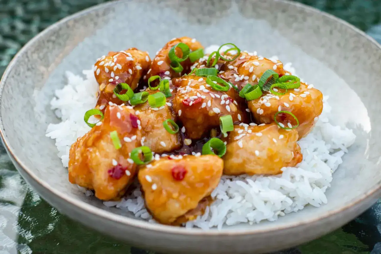 Krispig orange chicken med sesamfrön och salladslök, serverad över fluffigt vitt ris. En härlig rätt som passar alla.