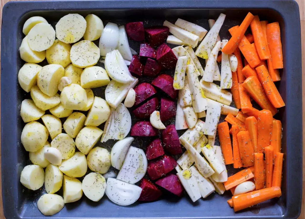 Ugnsrostade rotfrukter: potatis, mor&ouml;tter, palsternacka, r&ouml;dbetor och l&ouml;k, kryddade och redo f&ouml;r ugnen.