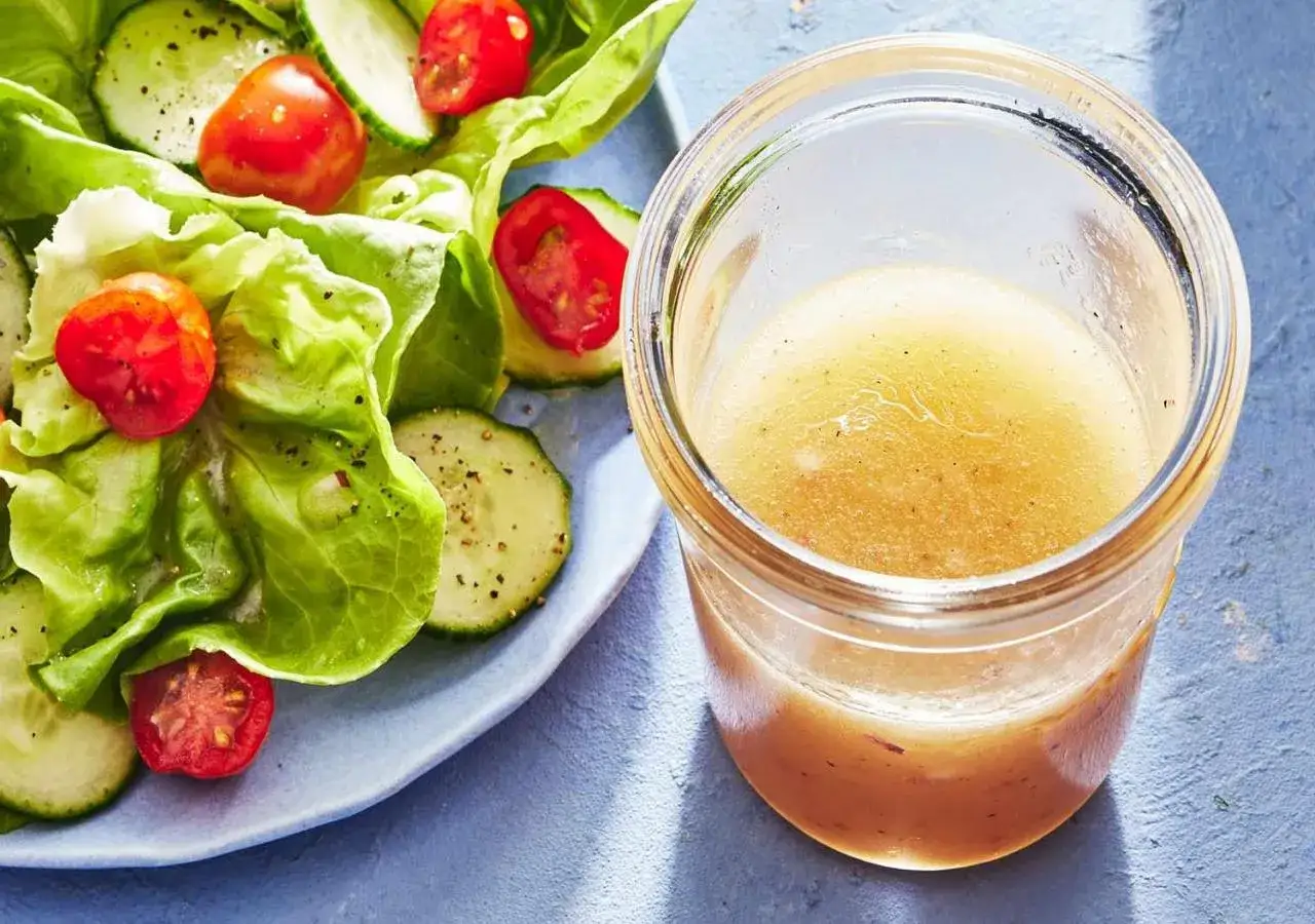 En burk med hemlagad salladsdressing bredvid en fräsch sallad med gurka och tomater. Ett perfekt salladsdressing recept för en god måltid.