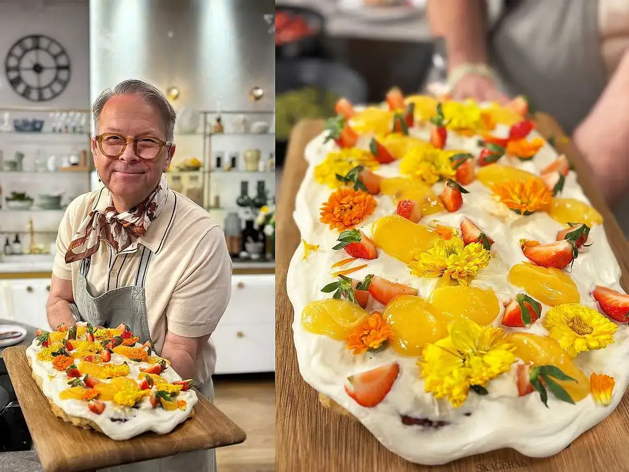 Glad kock visar upp en vacker påsktårta i långpanna, dekorerad med jordgubbar, aprikoser och gula blommor.