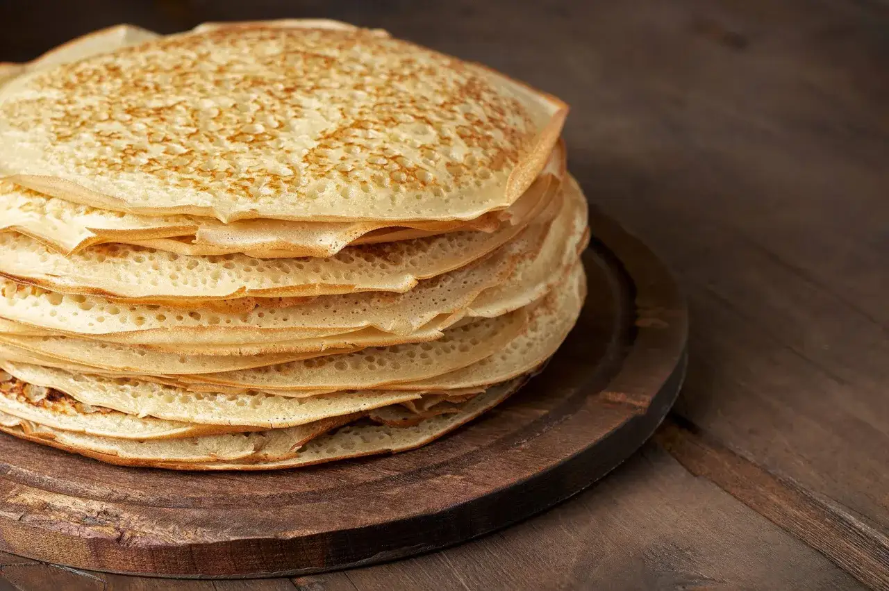 En hög med gyllene, tunna pannkakor på en träbricka. Perfekt för ett enkelt pankakor recept.