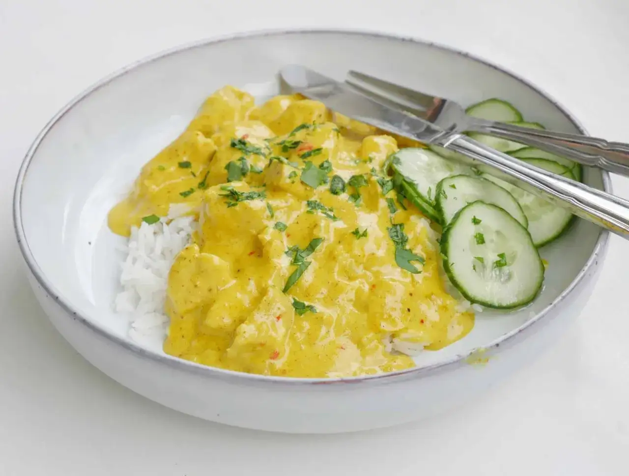 En sk&aring;l med ris t&auml;ckt av kr&auml;mig kyckling currys&aring;s, garnerad med f&auml;rsk persilja och skivad gurka. En uts&ouml;kt m&aring;ltid!