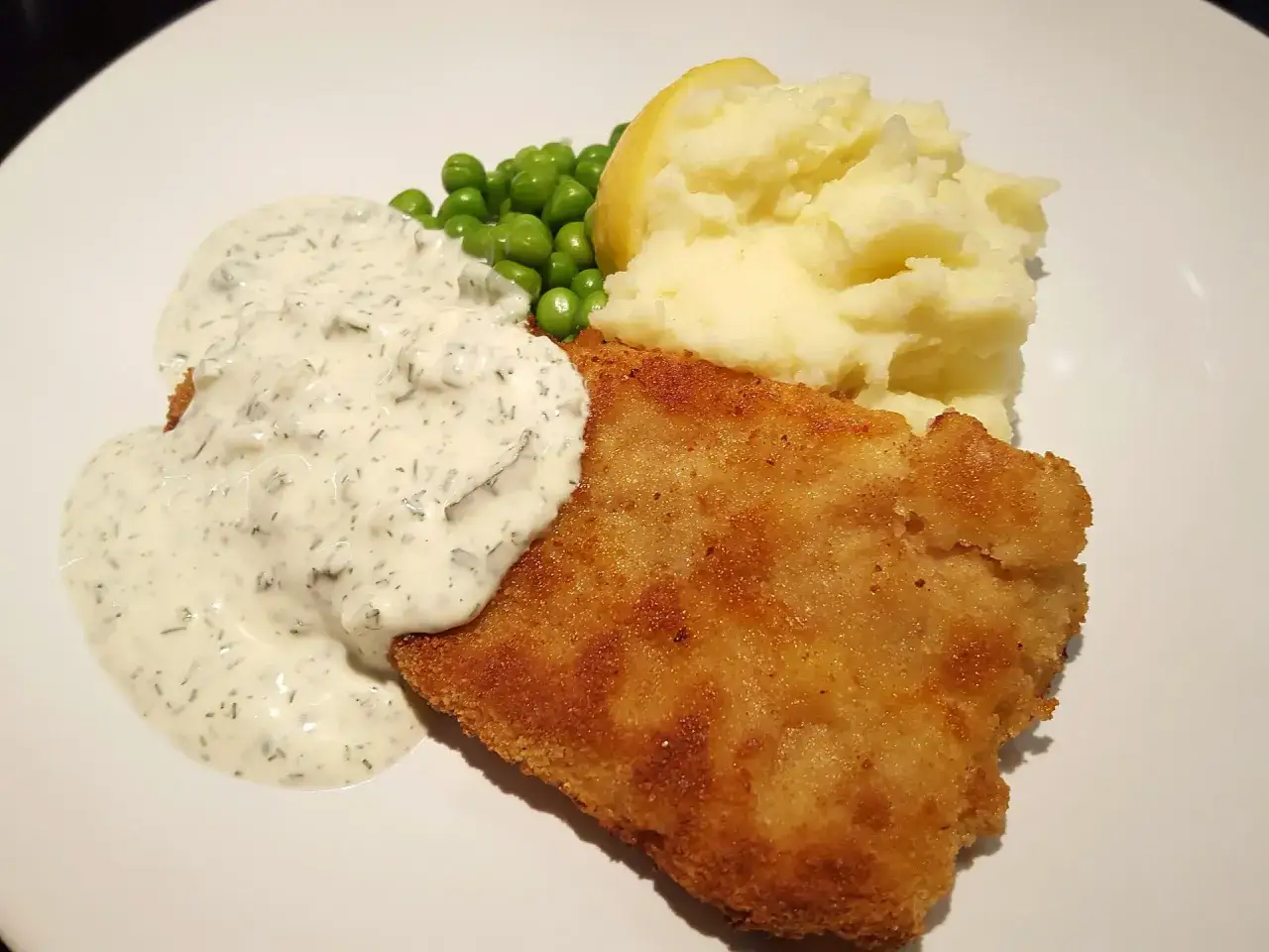 Panerad fisk med kr&auml;mig kall s&aring;s till panerad fisk, potatismos, &auml;rtor och en citronklyfta. En klassisk och god m&aring;ltid.