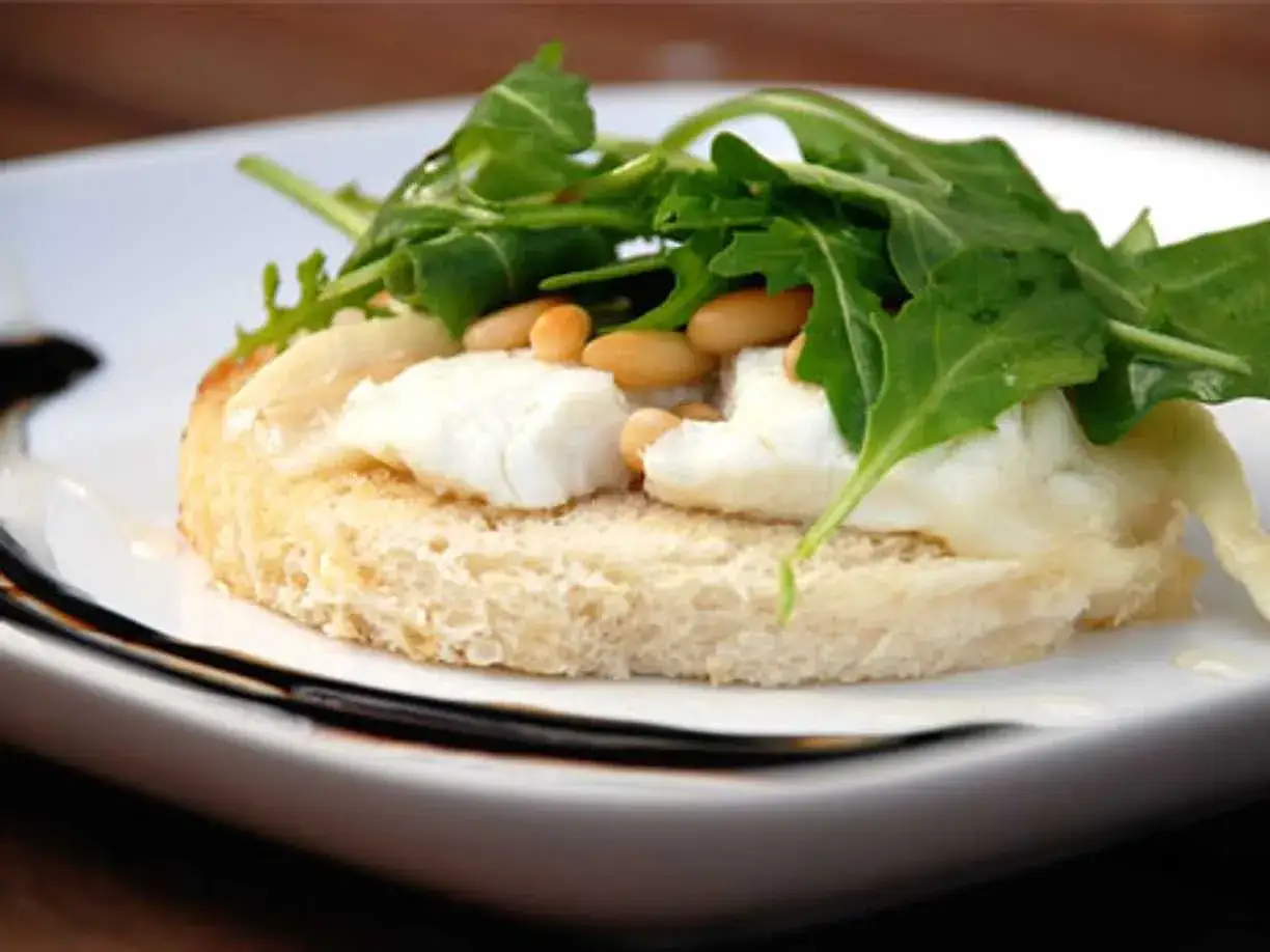 En bit rostat bröd med smält chevre chaud, pinjenötter och ruccola. En läcker förrätt.