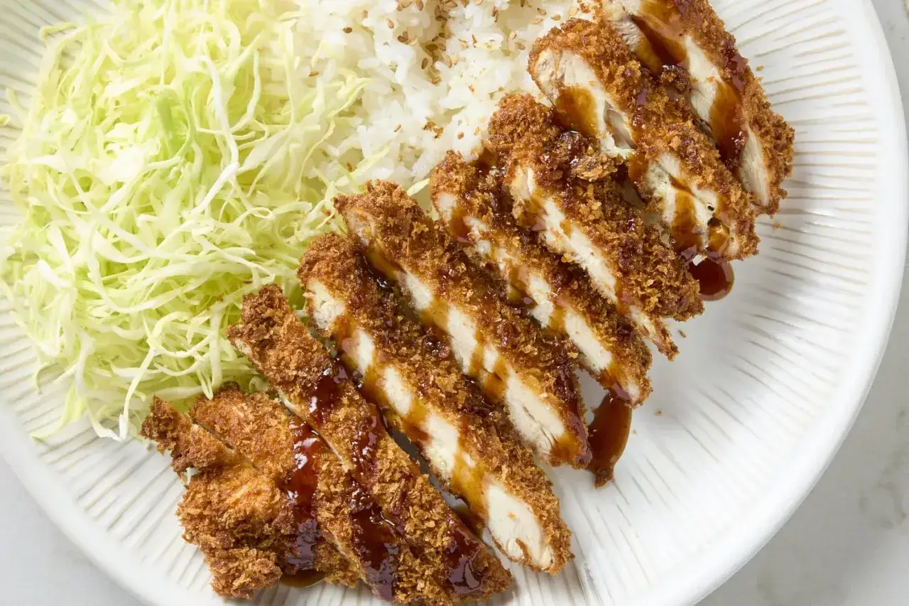 Krispigt kyckling katsu med ris och strimlad kål, allt serverat på en vit tallrik med en fin textur.