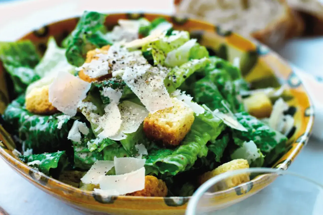 En skål med krispig romansallad, krutonger och parmesan, perfekt täckt med caesarsallad dressing.
