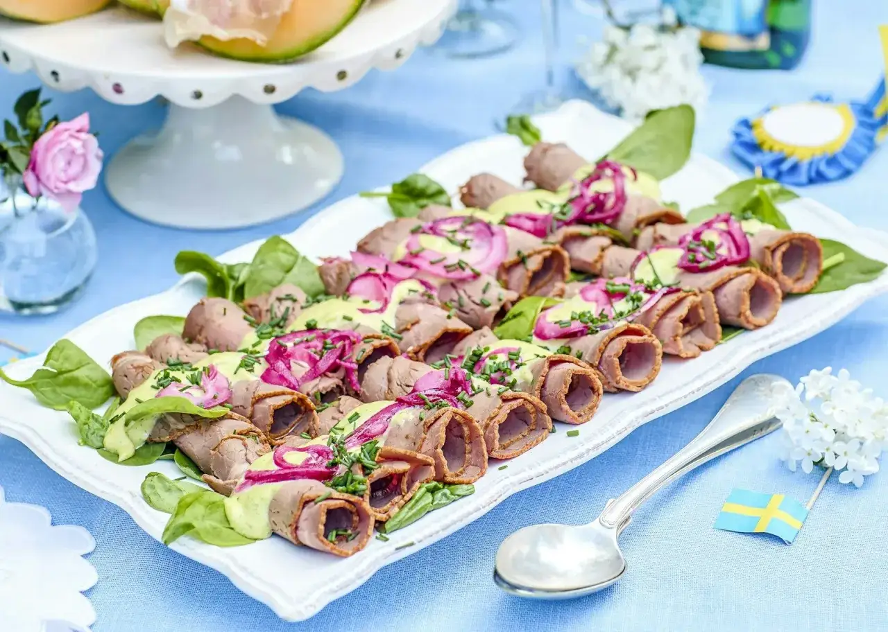 Rullad rostbiff med gr&ouml;n s&aring;s och r&ouml;dl&ouml;k, perfekt som enkel buff&eacute;mat till m&aring;nga. Serveras p&aring; en vit bricka med gr&ouml;na blad.