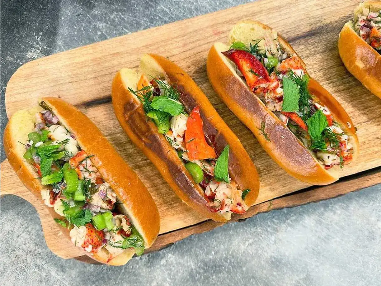 Tre l&auml;ckra lobster rolls fyllda med saftig hummer, krispig selleri och f&auml;rska &ouml;rter, serverade p&aring; ett tr&auml;fat.