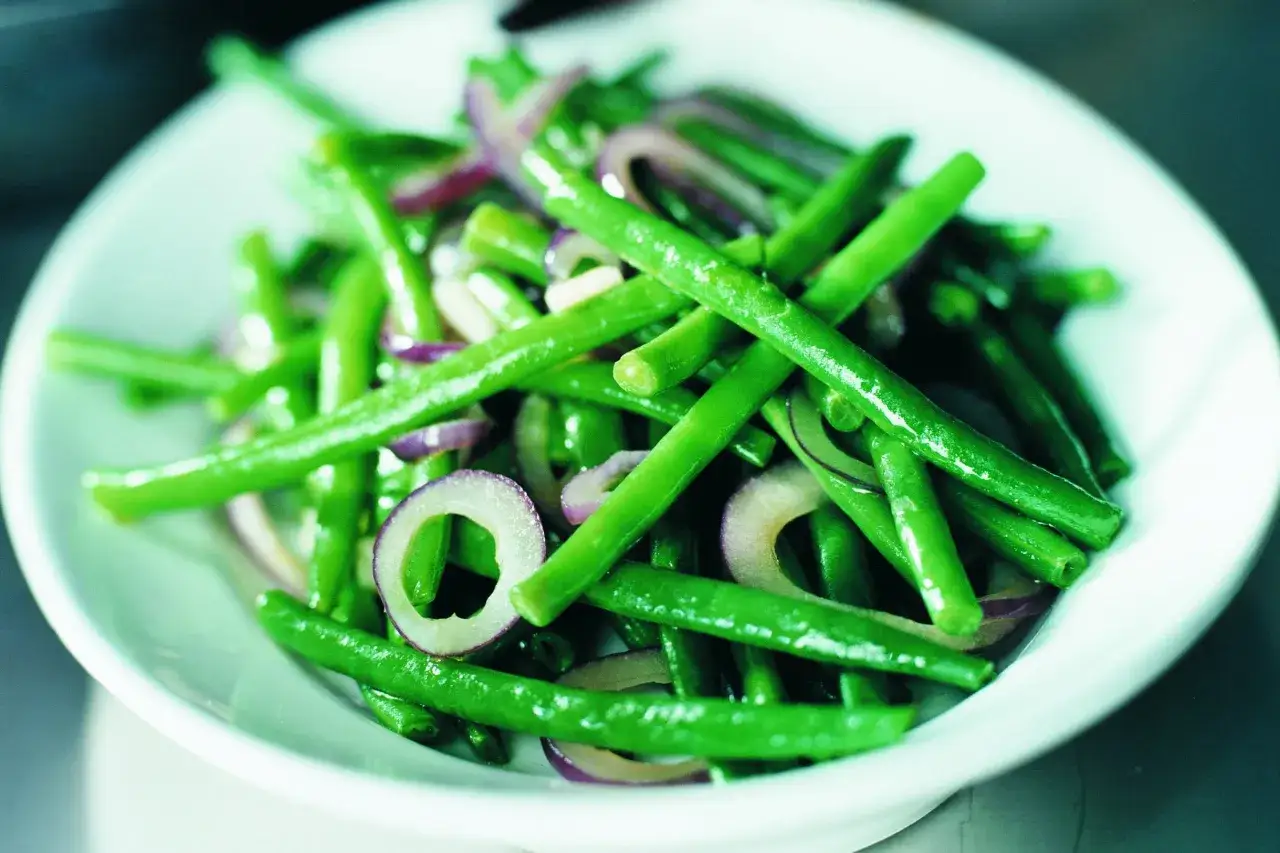 En skål med fräscha haricots verts blandade med tunna skivor rödlök.