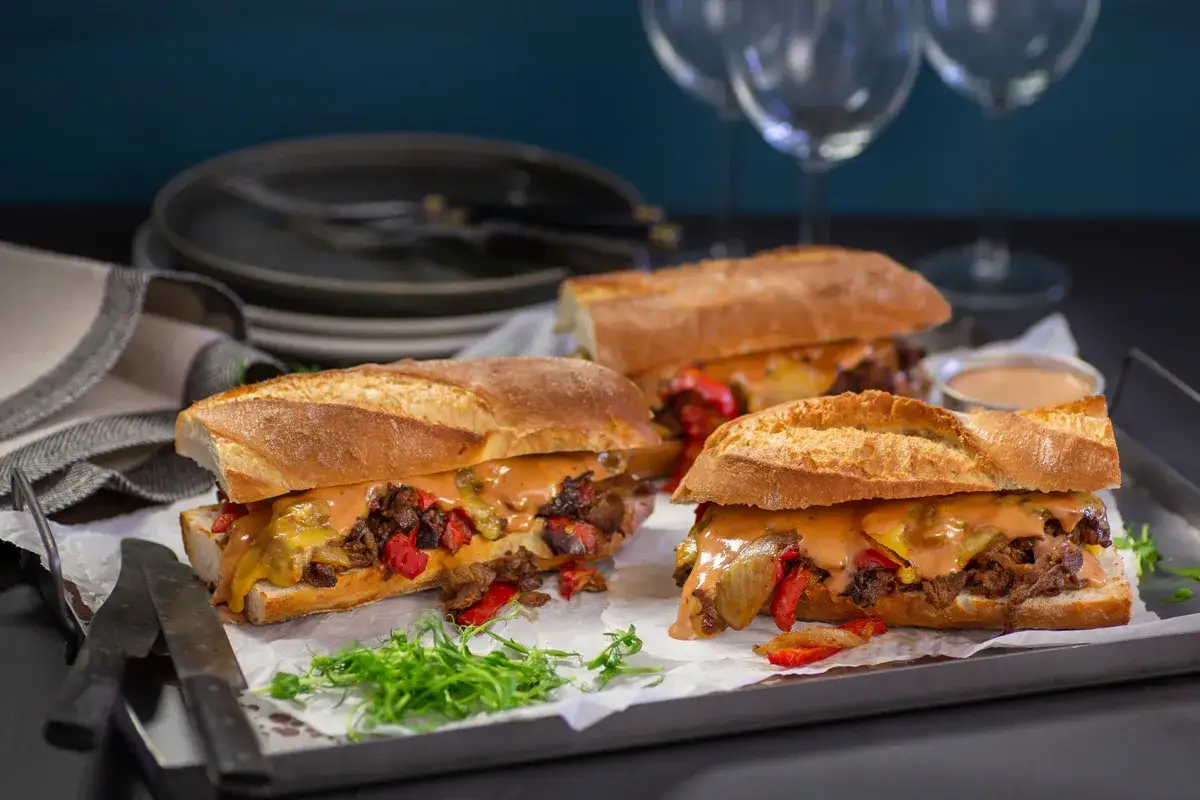 Tre saftiga steak sandwich med smält ost och grönsaker på en bricka, redo att avnjutas.