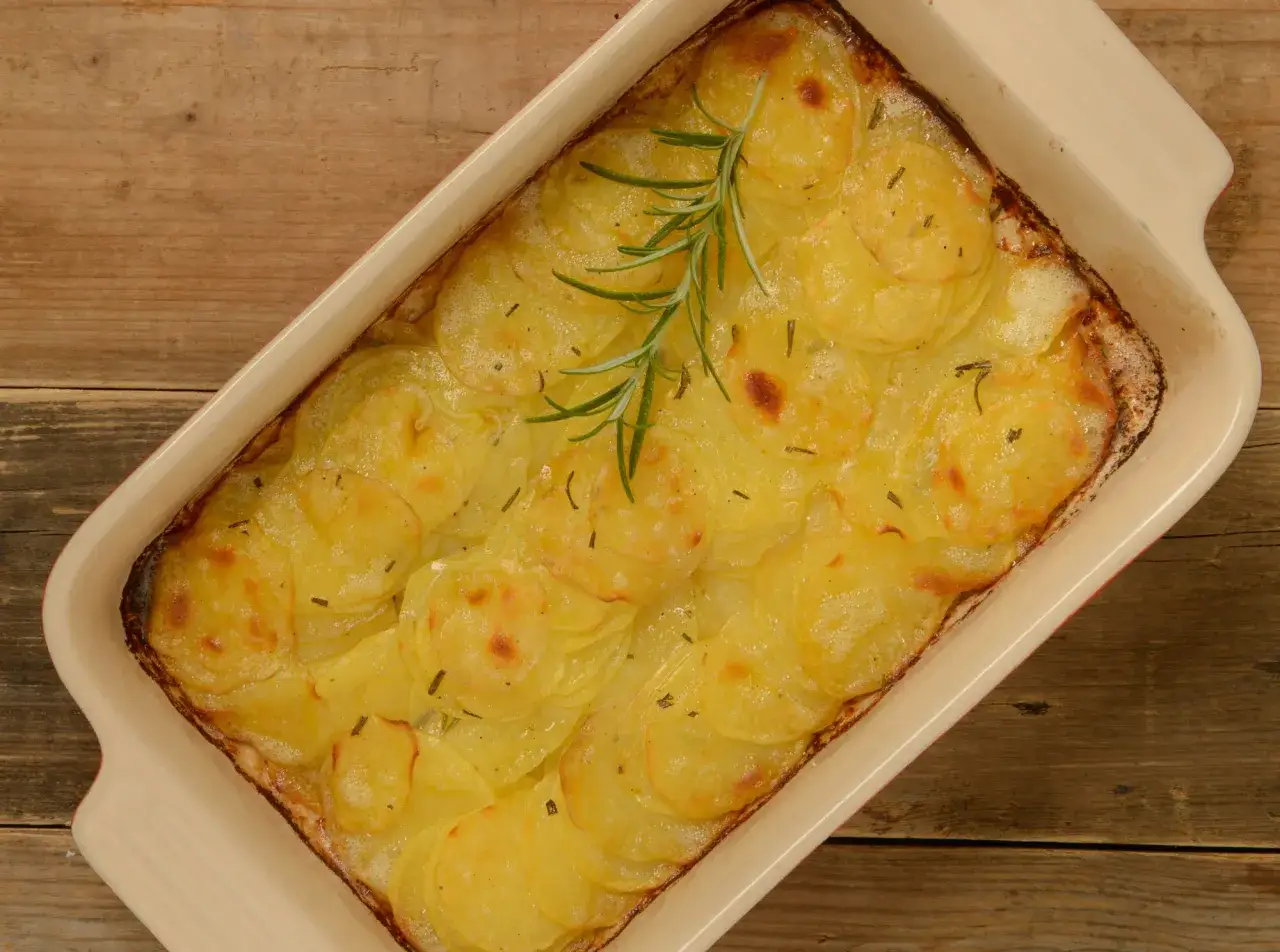 En ugnsform med gyllene, tunna potatisskivor, en klassisk pommes anna, toppad med en rosmarinkvist.