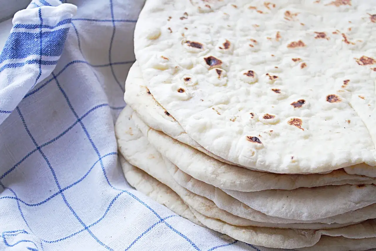 En h&ouml;g med nybakade tortillabr&ouml;d, perfekta f&ouml;r ditt n&auml;sta tortilla recept. Bredvid ligger en bl&aring;rutig k&ouml;kshandduk.