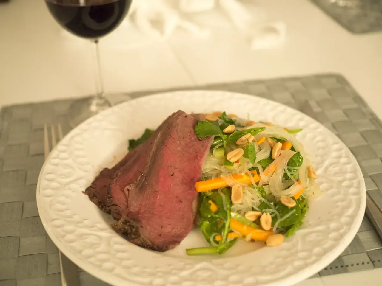 En saftig stek serveras med en fräsch asiatisk biffsallad med glasnudlar, grönsaker och jordnötter. Ett glas rödvin står bredvid.