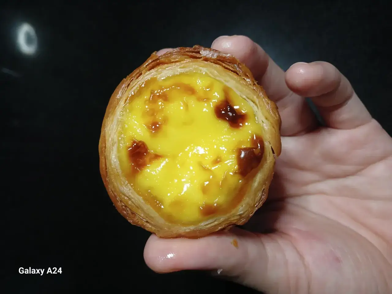 En hand håller en gyllene, krispig pastel de nata med krämig vaniljkräm och karamelliserade toppar.