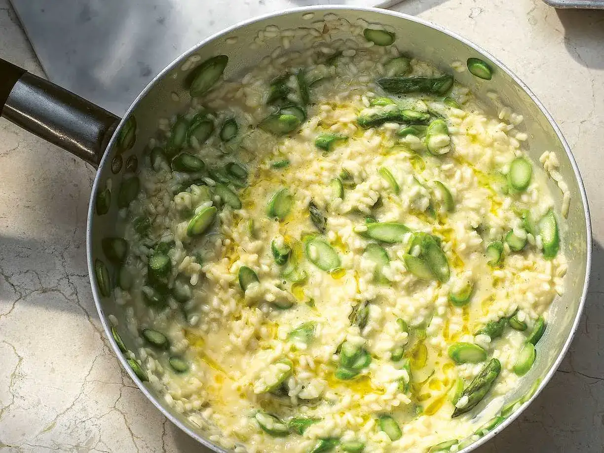 Kr&auml;mig sparris risotto i en panna, med f&auml;rska gr&ouml;na sparrisbitar och en gyllene olja som gl&auml;nser.